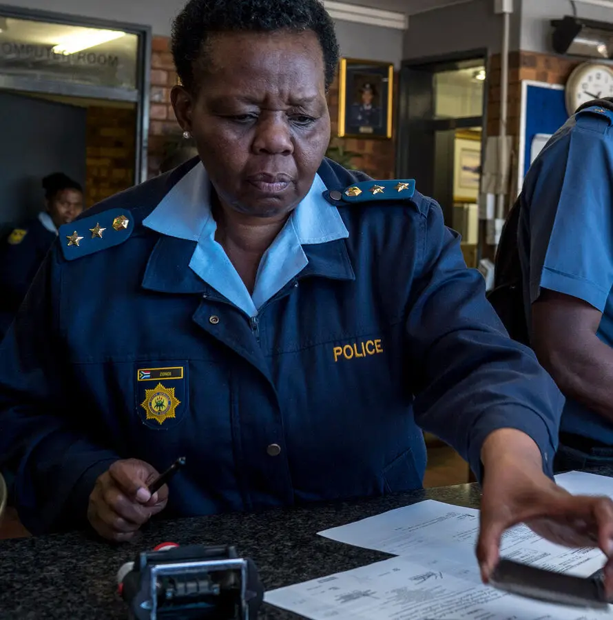 A South African police officer processing paperwork for a police clearance certificate application, relevant for South Africans applying from Canada.