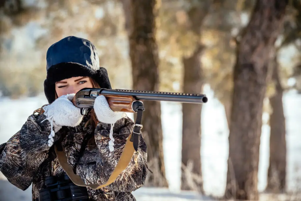 A young woman aiming a shotgun in the snow, demonstrating safe firearm handling in Canada.