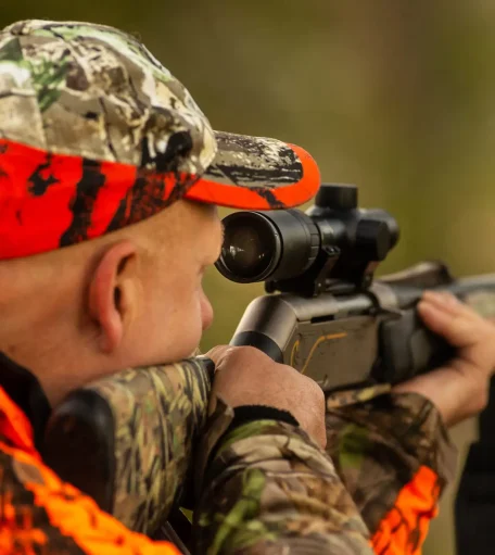 A hunter aiming a rifle in the bush, demonstrating legal and responsible firearm use in Canada.